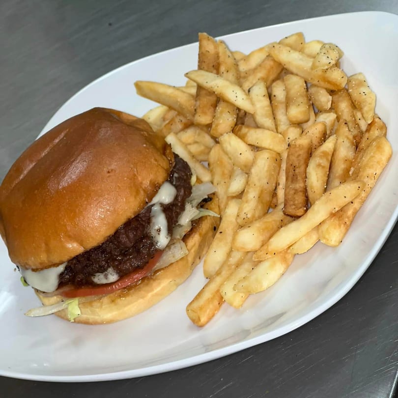 A juicy burger with melted cheese, lettuce, and tomato, served with a side of seasoned fries.