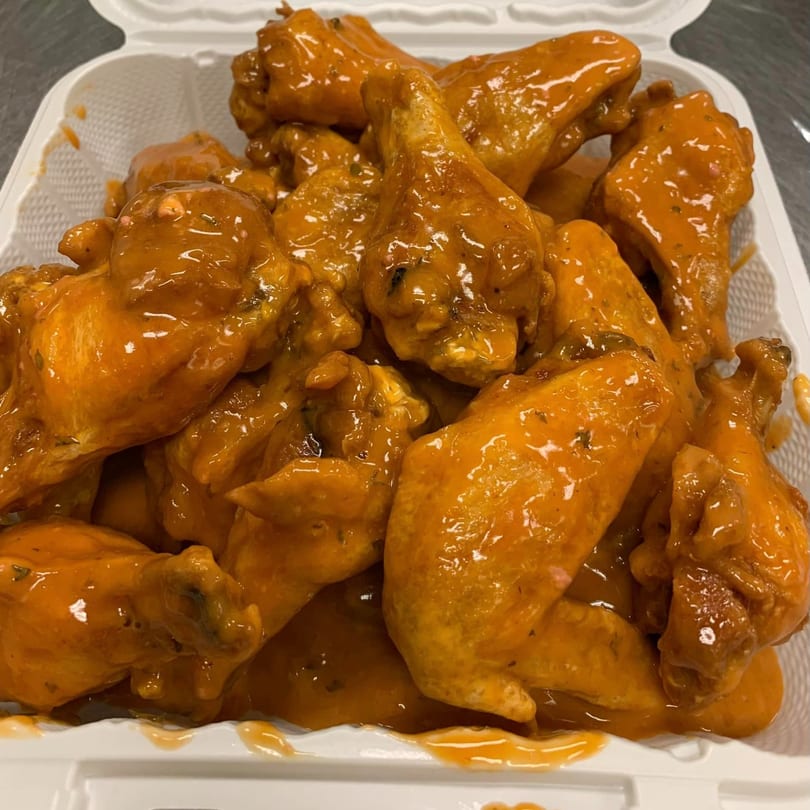 A white takeout container filled with American Pie of Rome's buffalo wings, coated in orange sauce.