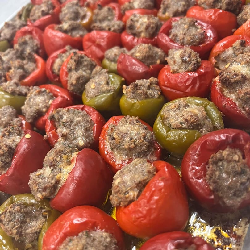 Close-up of red and green stuffed peppers with a savory meat filling, glistening with oil.