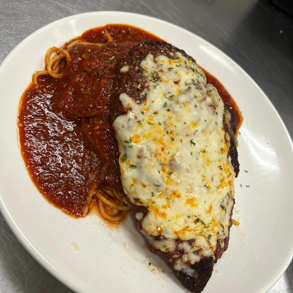 Chicken parmesan with melted cheese and spaghetti in red sauce on a white plate.