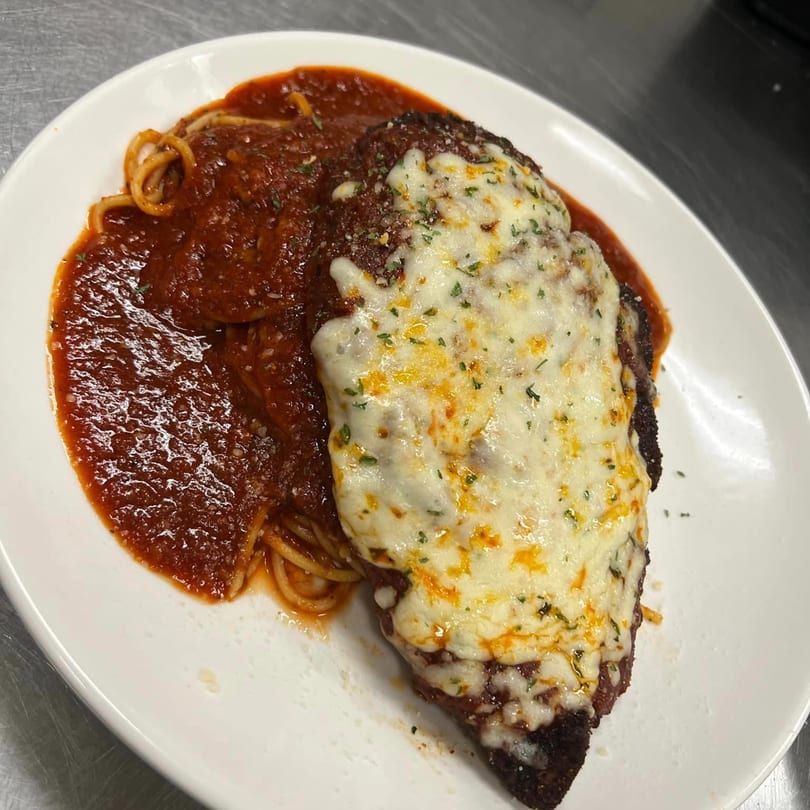 Chicken parmesan with melted cheese and spaghetti in red sauce on a white plate.